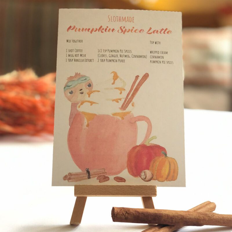 Pumpkin Spice Rezept auf Postkarte mit Faultier auf Staffelei stehend vor unscharfem Hintergrund